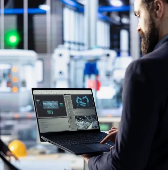 Profesional en entorno industrial analizando datos en un portátil con robots y maquinaria de fondo, representando los beneficios del residuo cero en la eficiencia operativa y productividad empresarial