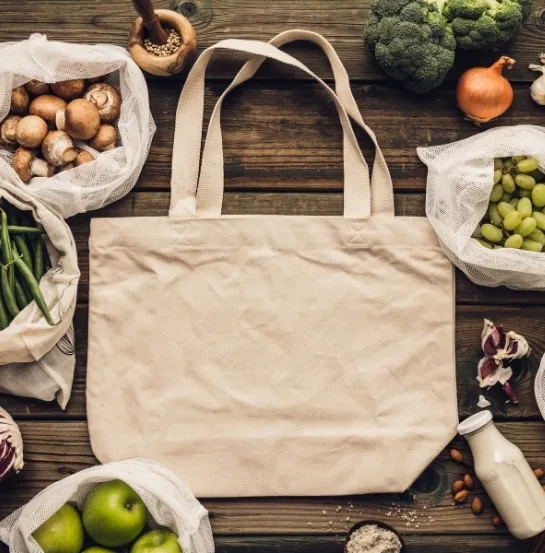 Bolsa de tela reutilizable rodeada de alimentos frescos y bolsas de malla para compra a granel, representando el origen del movimiento residuo cero en los hábitos de consumo cotidianos