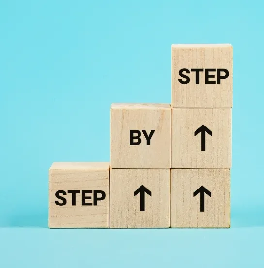 Bloques de madera apilados en escalera con el mensaje Step by Step y flechas hacia arriba, representando el avance gradual hacia el estilo de vida residuo cero