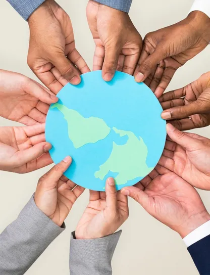 Manos diversas de profesionales sosteniendo juntas un globo terráqueo de papel, simbolizando el compromiso colectivo de las empresas con la sostenibilidad global