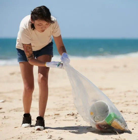 Voluntaria recogiendo residuos plásticos en una bolsa durante una limpieza de playa, representando la RSC como inversión a largo plazo para la empresa y la sociedad
