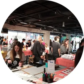 Participantes en una sesión presencial de formación híbrida en sostenibilidad, con mesas de trabajo, materiales y actividades prácticas en un espacio amplio y dinámico