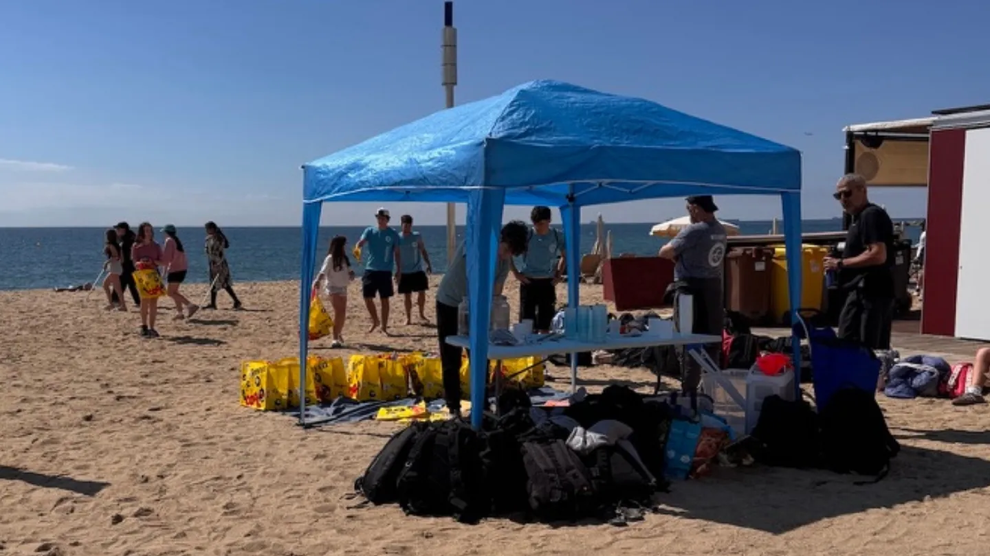 Grupo de estudiantes y voluntarios organizándose bajo una carpa azul en la playa durante una limpieza de costa organizada por Go Zero Waste con la Escola Pia Sarrià-Calassanç