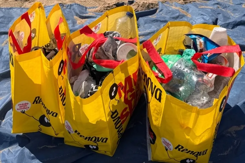 Tres bolsas amarillas llenas de residuos recogidos durante una limpieza de playa organizada por Go Zero Waste con la Escola Pia Sarrià-Calassanç
