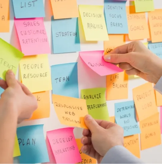 Manos colocando post-its de colores con palabras como estrategia, equipo y objetivos en una pared, representando la fase de planificación de un team building sostenible
