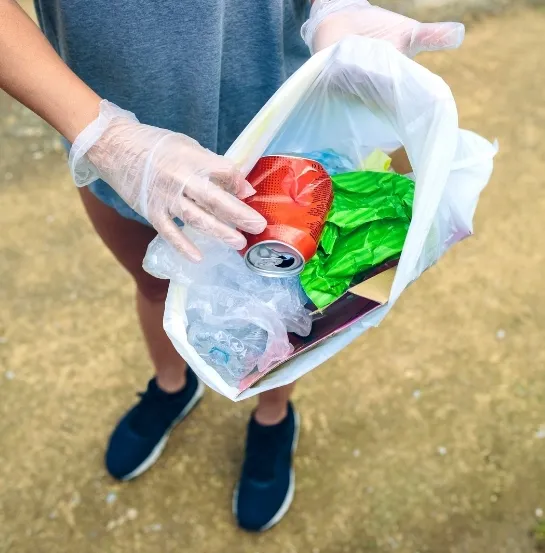 Persona sosteniendo una bolsa con latas, plásticos y otros residuos recogidos durante una sesión de plogging al aire libre