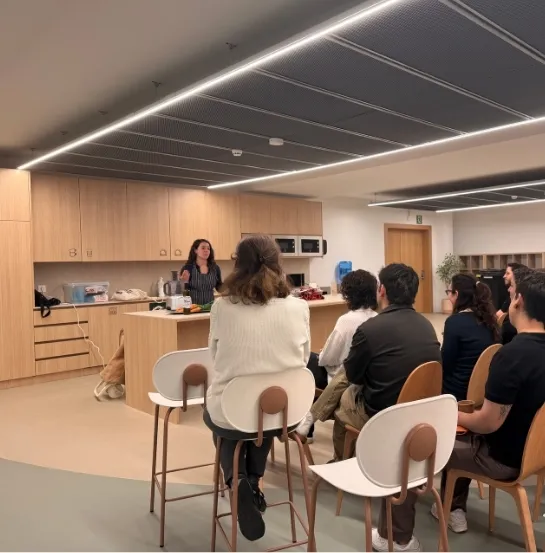 Formadora impartiendo un showcooking de cocina de aprovechamiento ante un equipo sentado en una cocina corporativa moderna, actividad de team building sostenible de Go Zero Waste