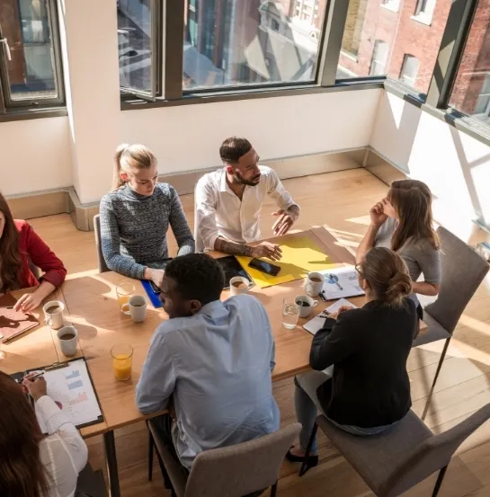 Equipo diverso de profesionales reunido alrededor de una mesa de trabajo con documentos y dispositivos, representando la planificación de la formación FUNDAE en una empresa