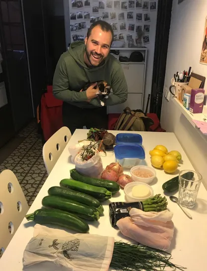 Hombre sonriente en casa con verduras frescas y compra realizada en bolsas de tela y envases reutilizables