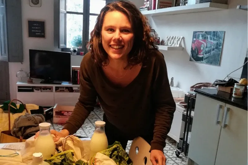 Mujer sonriente en la cocina con la compra realizada sin envases: leche en botellas de vidrio y verduras frescas