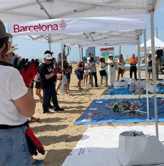 Equipo empresarial participando en una actividad de limpieza de playa en Barcelona bajo una carpa institucional, con residuos recogidos visibles, como ejemplo de formación ambiental experiencial