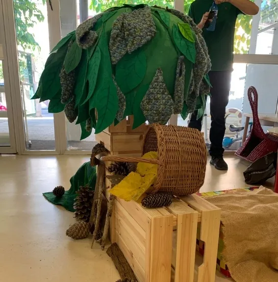 Handmade tree set with fabric leaves, pine cones and a basket on wooden crates, props from the 3Rs storytelling activity
